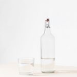 rocks glass beside half empty bottle on white surface